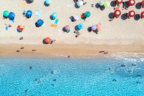 Preview: Aerial view of colorful umbrellas on sandy beach, swimming people in blue sea on summer sunny day
