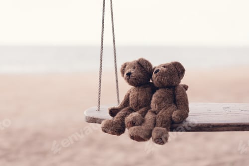 Preview: Two brown teddy bears so cute sitting on wooden swing looking to the sea in romantic moment.