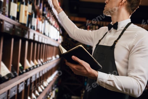 Preview: Male cavist examines the bottles with wine and making notes at his notepad