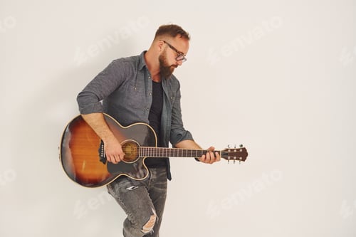 Preview: Standing in the studio. Man in casual clothes and with acoustic guitar is indoors