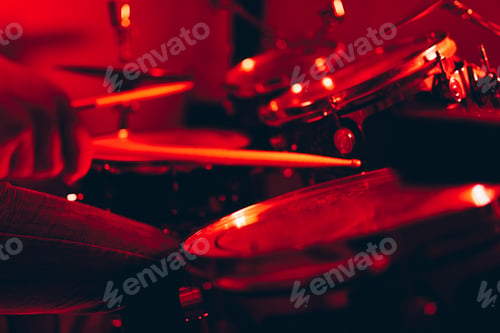 Preview: Anonymous man with drumsticks playing on drums in redness