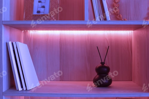Preview: On a shelf with pink neon lighting there is a small black ceramic vase with two aroma sticks