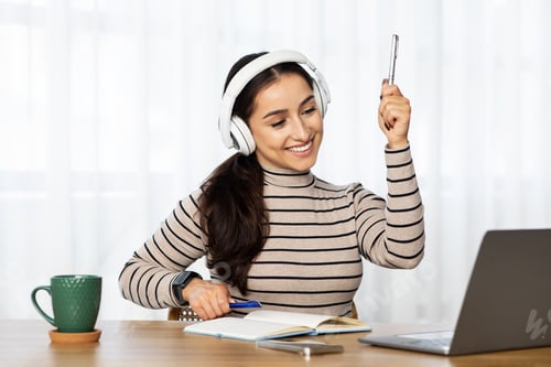 Preview: Glad young arab woman teacher work at computer, in wireless headphones, raise hand