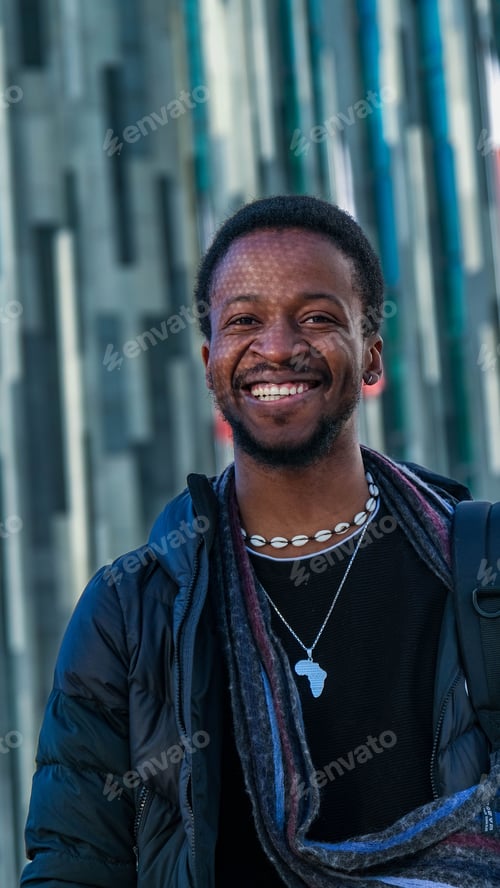 Preview: Young African man in a black outfit walking in a street posing in front of a glass paneled building