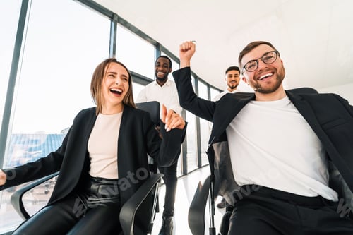 Preview: Joyful employees ride on chairs around the office celebrating the end of the working week