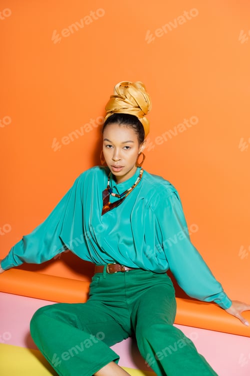 Preview: Well dressed african american model looking at camera while sitting on colorful background
