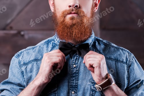 Preview: An important detail of retro style. Close-up of handsome young bearded man adjusting his bow tie