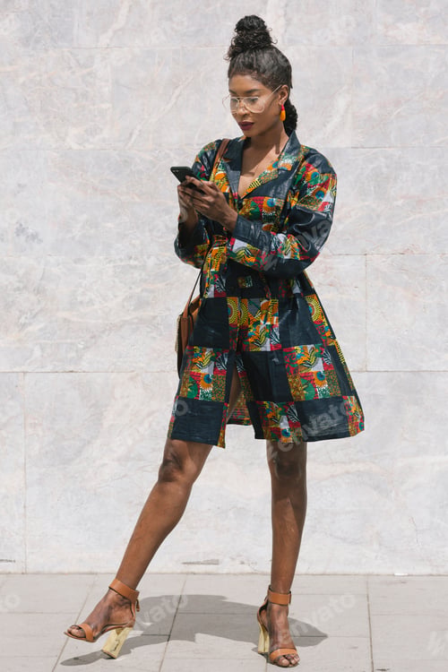 Preview: Portrait of chic woman wearing patterned dress using cell phone