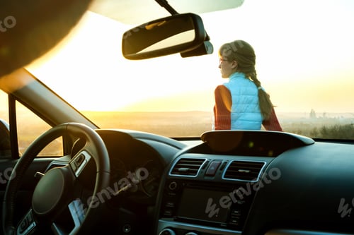Preview: Young woman standing near her car enjoying warm sunset view.