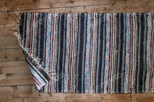 Preview: Multicolored carpet with a curled edge on an old wooden floor, indoors. Top view.