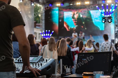 Preview: low light, professional DJ music mixer, laptop at party festival with crowd of people in background