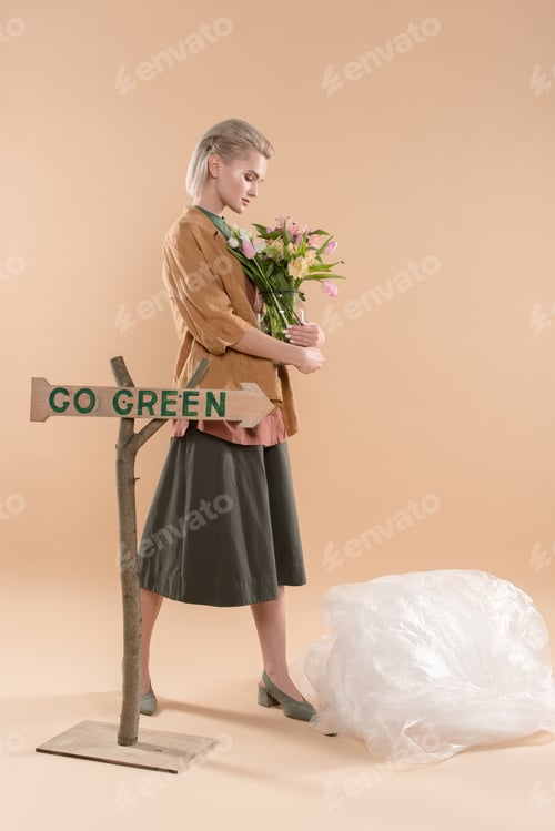 Preview: blonde girl in eco clothing holding vase with flowers near sign with go green lettering on beige