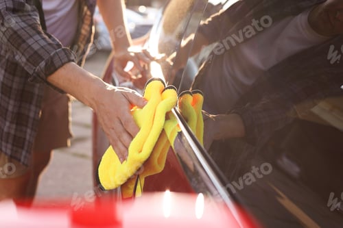 Preview: Man wiping car with yellow microfiber rag outdoors, closeup