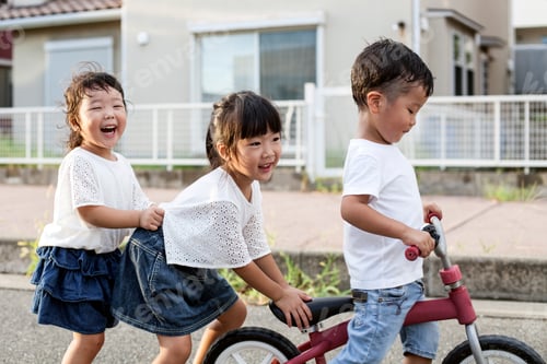 Preview: Portrait of two Japanese girls and boy playing on street with a bicycle, smiling at camera.