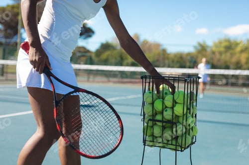 Preview: Midsection of female african american player practicing tennis at court on sunny day