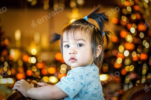 Preview: A happy child looks away through the camera on Christmas evening against the background of lights ga