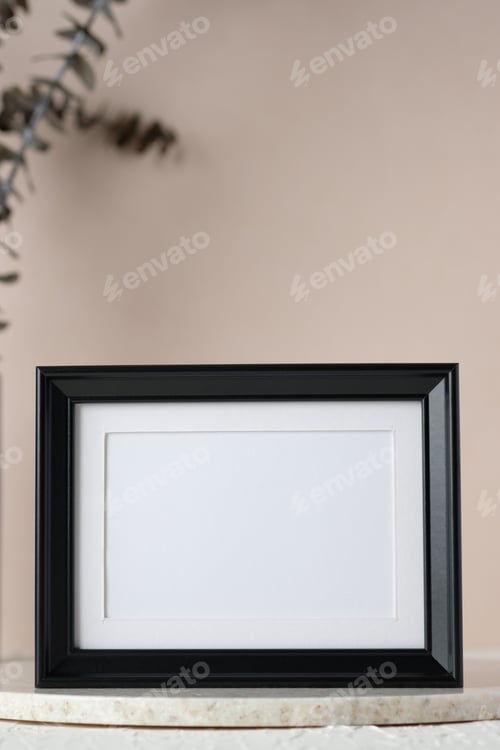 Preview: blank black photo frame mockup with eucalyptus brancch at peach wall