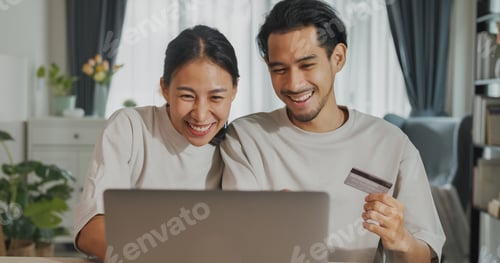 Preview: Asian couple sit on couch with laptop success credit card payment online shopping at home on holiday