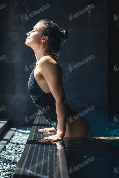 Preview: Attractive young woman in a black swimsuit is relaxing in the pool.