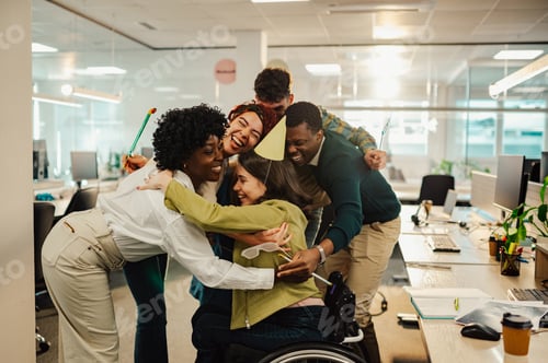 Preview: Diverse colleagues hugging birthday girl who uses a wheelchair at the office.