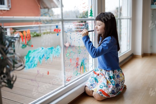 Preview: Cute little girl drawing merry christmas wishes on window