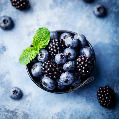Preview: Blueberry and Blackberry Berries with Mint Leaves in Black Bowl on Blue Stone Background.