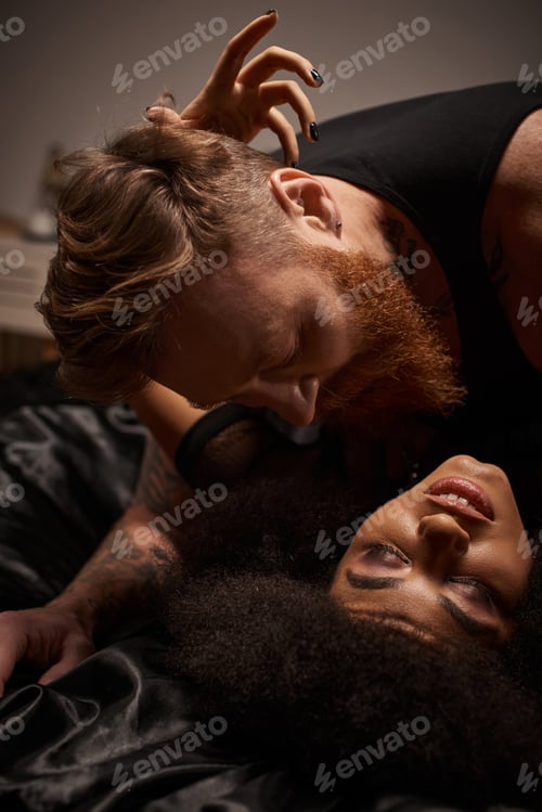 Preview: passionate moment of multicultural couple making love on bed, man looking at african american woman