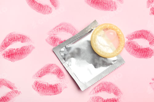 Preview: Condom with lipstick kiss marks on pink background, flat lay. Safe sex