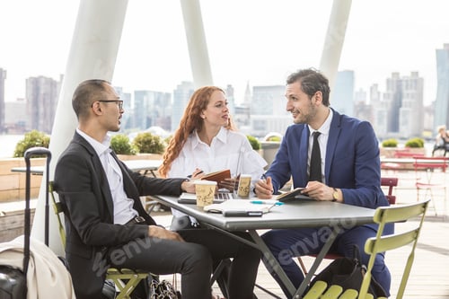 Preview: Businessmen and woman meeting at waterfront cafe with New York skyline, USA