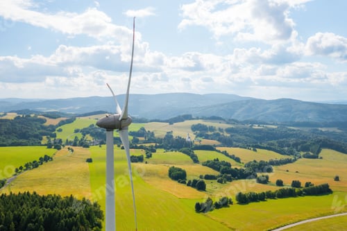 Preview: Aerial view of wind turbines propeller in the yellow field with amazing view on the mountains