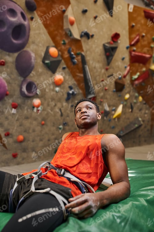Preview: vertical shot of relaxed african american man after climbing rock wall chilling on crash pad