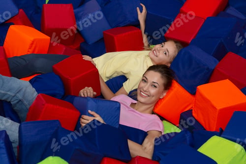 Preview: Cheerful young mom with adorable teen daughter lying at indoor foam cube pit, playing together in