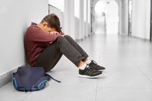 Preview: Sad school boy sitting alone on floor at corridor