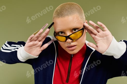 Preview: A young bald woman in vibrant attire poses confidently in a stylish urban setting