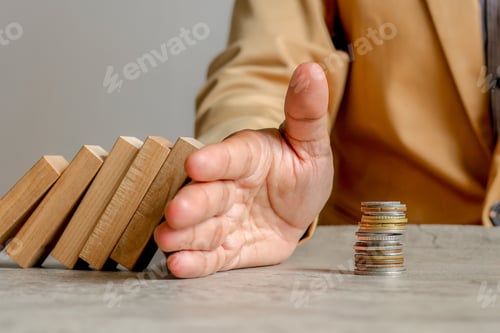 Preview: Close Up Of Hand Stops Falling Dominoes From Hitting Stacked Coins Symbol Of Financial Protection