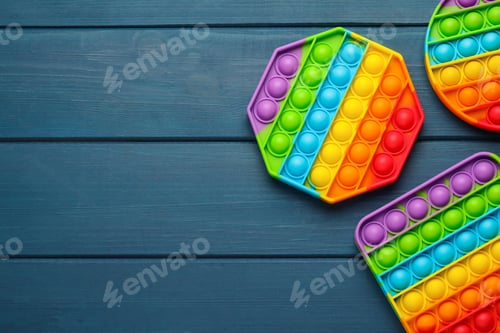 Preview: Rainbow pop it fidget toys on blue wooden table, flat lay. Space for text