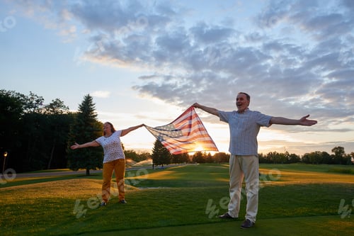 Preview: Man and woman holding usa flag outdoors.