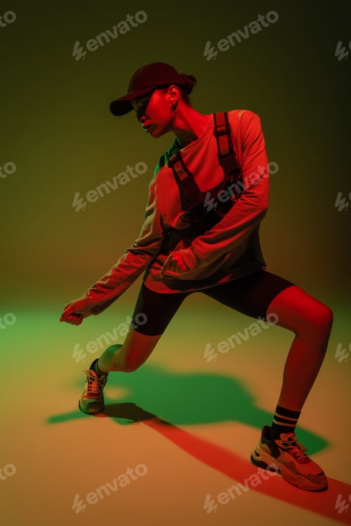 Preview: full length of african american woman in sweatshirt and vest posing on green with red light