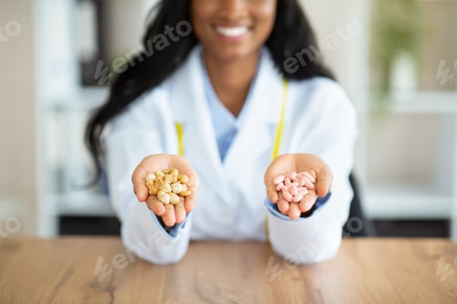 Preview: Healthy nutrition vs medication. Unrecognizable black dietitian holding tablets and nuts at table in