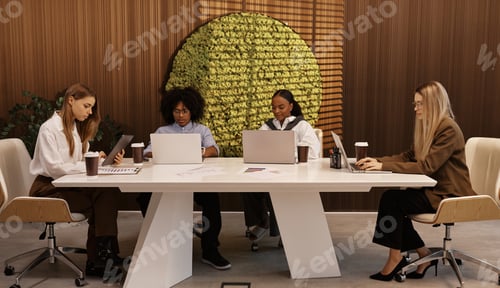 Preview: Modern diverse team working together at office table with laptops and coffee