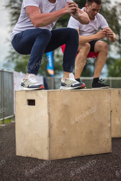 Preview: Two male athletic friends doing box jump outdoor on top of the mountain.