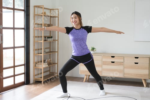Preview: Young asian woman doing yoga balance exercise with warrior pose for healthy lifestyle at home