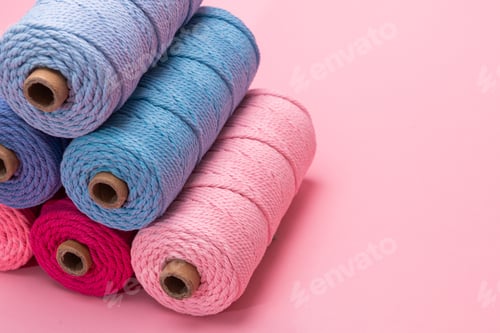 Preview: Stacked spools of macrame yarn in pink and blue tones arranged against a soft pink background