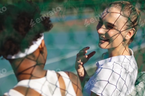 Preview: Happy caucasian female tennis player talking with african american athlete during break at court