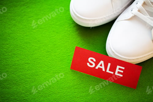 Preview: Pair of new stylish white sneakers with discount on green background.