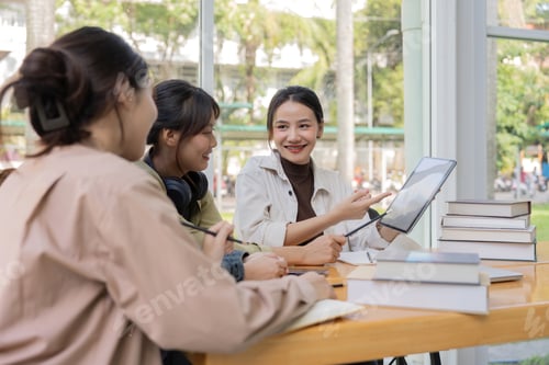 Preview: University students sitting together at table with book and laptop. Happy young people doing group