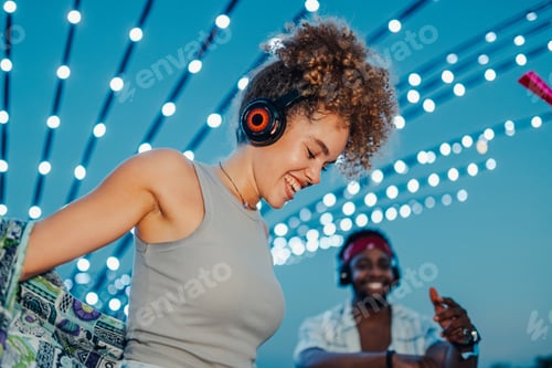 Visualização: Jovem mulher dançando com fones de ouvido no festival de música com um amigo