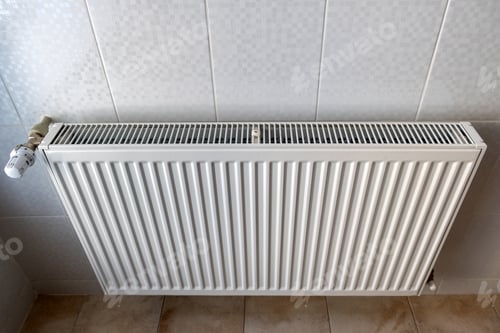 Preview: White metal heating radiator mounted on a wall in room interior.