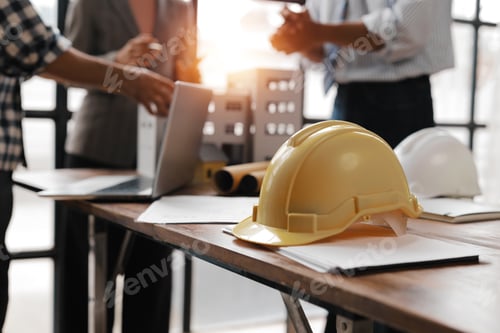 Preview: Yellow safety helmet resting on documents on architect's desk during meeting