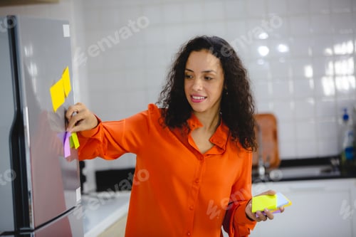 Preview: Young and organized female with curly hair in casual clothing making to-do and checklist